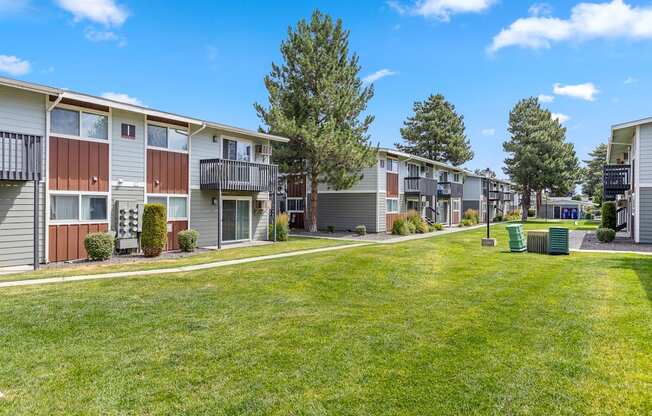 A row of apartment buildings with green lawns in front A bedroom with a bed, nightstand, and window at Wildflower, Kennewick, WA 99336..