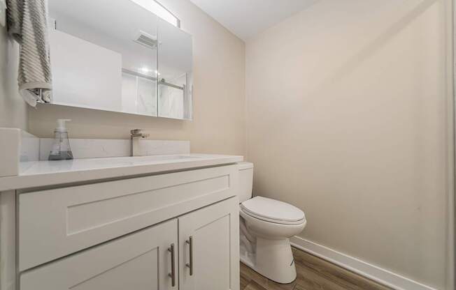 A white toilet sits in a bathroom with a white sink and a mirror above it.
