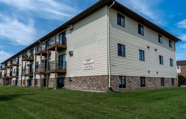 The exterior of a three level apartment building with a grass area out front