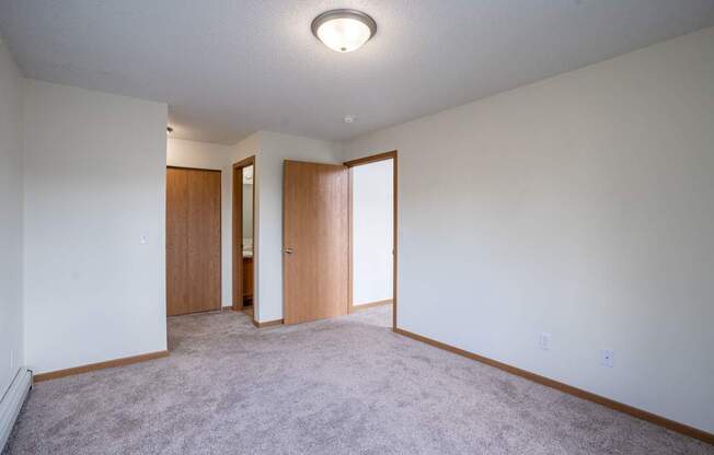 A room with a carpeted floor and two doors. Bismarck, ND Sierra Ridge Apartments