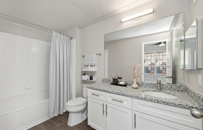 Model Bathroom with White Cabinets, Wood-Style Flooring and Shower/Tub at Chapel Hill Apartments in Lewisville, TX.