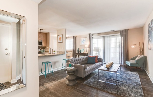 a living room with a couch a table and a chair and a kitchen in the background