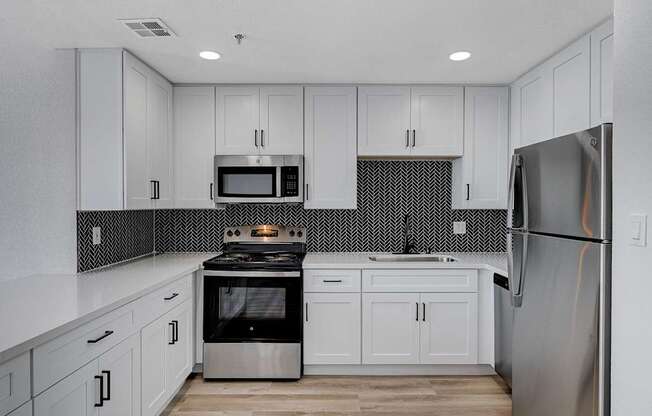 A kitchen with white cabinets and a black and white backsplash.