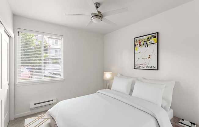 A bedroom with a bed, a ceiling fan, and a picture on the wall.