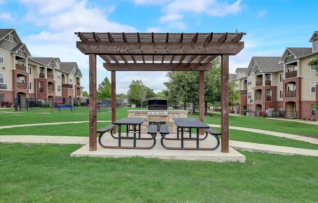 a picnic area with two picnic tables and a fire pit in the middle of a grassy