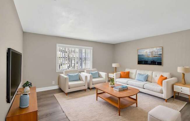 A living room with a white couch, a coffee table, and a television.