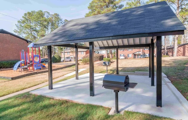 A pavilion with a black roof and a bench is situated in a grassy area.