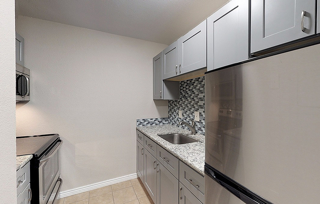 Modern kitchen with sleek gray cabinets, granite countertops, and stainless steel appliances featuring a stylish tile backsplash.