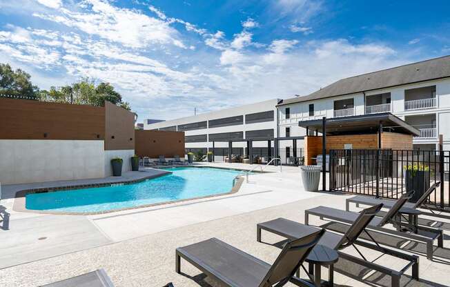 A pool area with sun loungers and a building in the background.