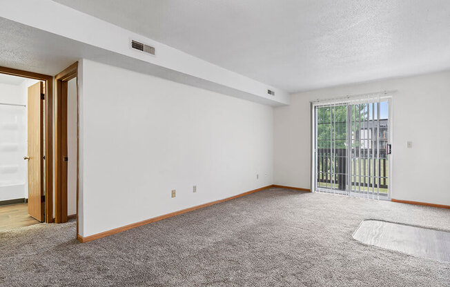 an empty living room with a sliding glass door to a balcony