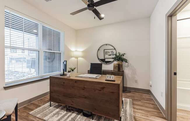 an office with a large window and a wooden desk and a ceiling fan at Meridian at CityPlace, Woodbury, MN
