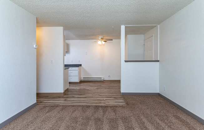 A room with a carpeted floor and a small kitchenette.
