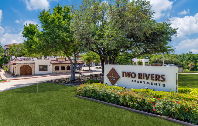 a sign for two rivers apartments in front of a garden and trees