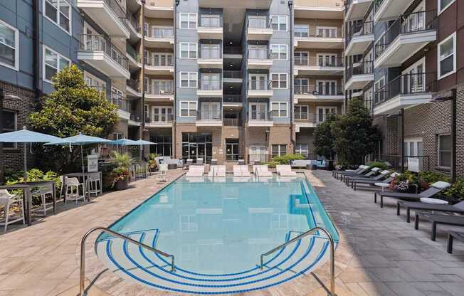 an outdoor swimming pool with lounge chairs and umbrellas in front of an apartment building
