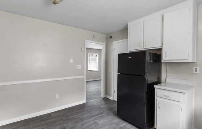 an empty kitchen with black refrigerator and white cabinets