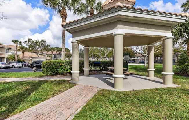 A gazebo with a tiled roof is surrounded by a grassy area and a brick walkway.