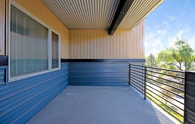 A balcony with a metal railing and a window with a view of trees.