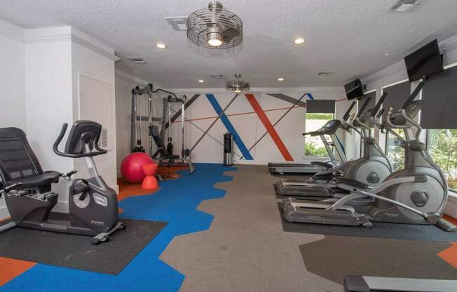 a gym with weights and cardio equipment and a wall with a geometric design