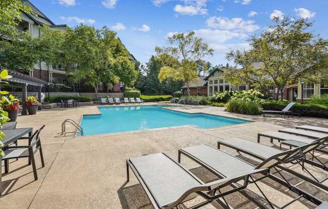 A pool surrounded by lounge chairs and trees.
