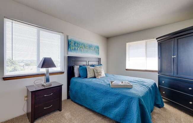 Bright bedroom in the two-bedroom model unit at Olde English Village, showcasing a large window and well-appointed furnishings.