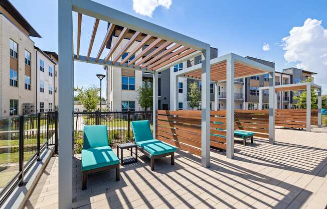 A patio with a white pergola and blue chairs.
