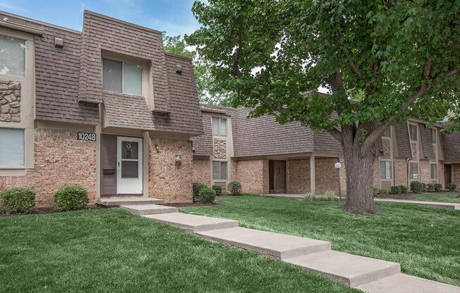 The exterior of an apartment building with a lush tree and walkway at Preston Court in Overland Park.