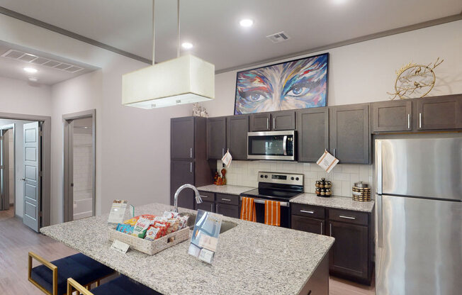Modern kitchen here at 49 West Apartments with dark cabinets, stainless steel appliances, and a central granite island. A vibrant eye painting adds color above the cabinets.