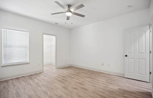 A room with a ceiling fan and light, hardwood floors, and white walls.