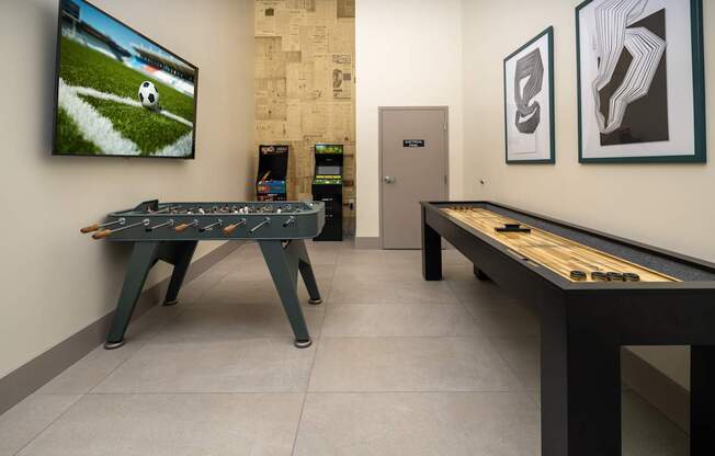 A room with a foosball table and a television showing a soccer game.