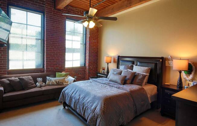 Lofts at Lafayette Square bedroom with exposed beams, ceiling fan, exposed brick exterior wall and light colored carpet