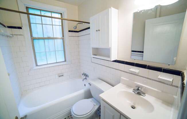bathroom with cabinet, tub, toilet, vanity, large mirror and window at 3101 pennsylvania apartments in washington dc