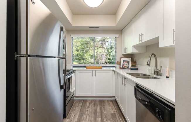a white kitchen with stainless steel appliances and a window