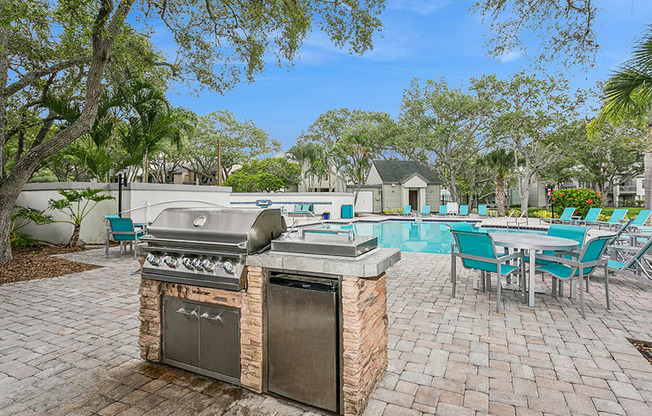 Outdoor BBQ Area with Lounge Furniture and View of Swimming Pool at Huntington Place Apartments located in Sarasota, FL.