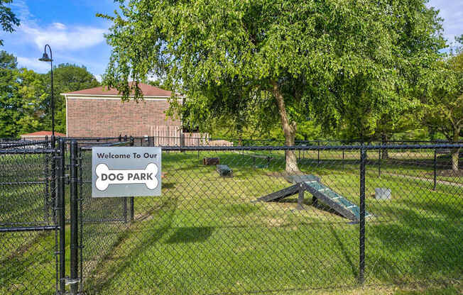 A dog park sign is on a fence in front of a brick building.