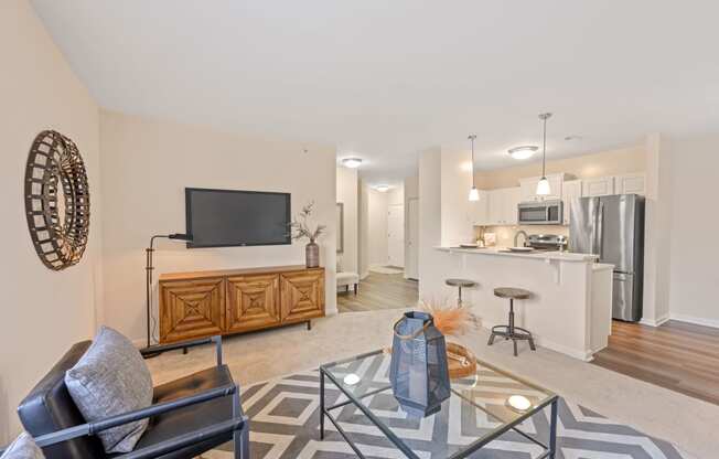 a living room with a glass coffee table and a kitchen in the background