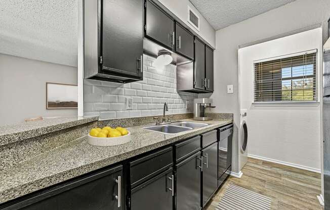 a kitchen with black cabinets and a counter top with a sink at Legacy Apartments in Plano, TX