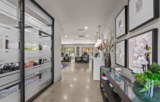 A modern interior with a long hallway, a glass table with flowers, and framed pictures on the wall.