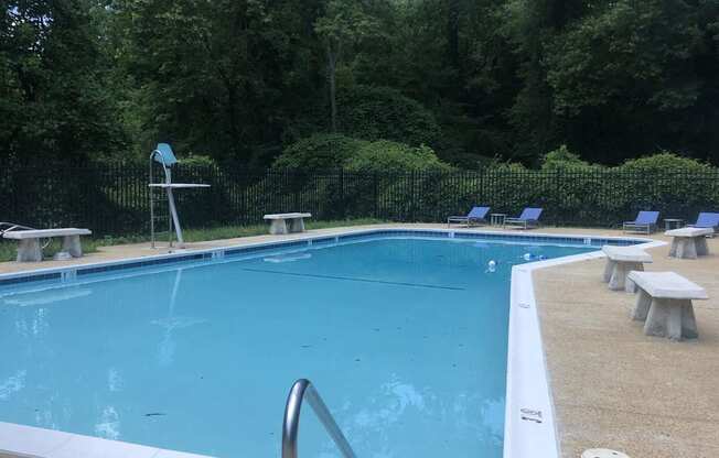 A swimming pool surrounded by trees and benches.