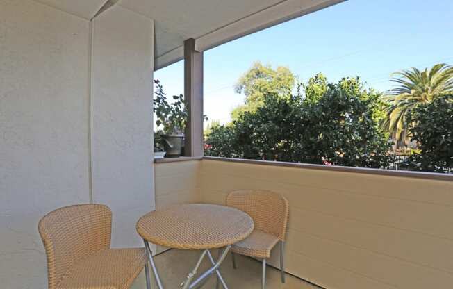 Apartment private patio with small table and two chairs overlooking trees on a sunny day at Pacific Sands, California, 92117