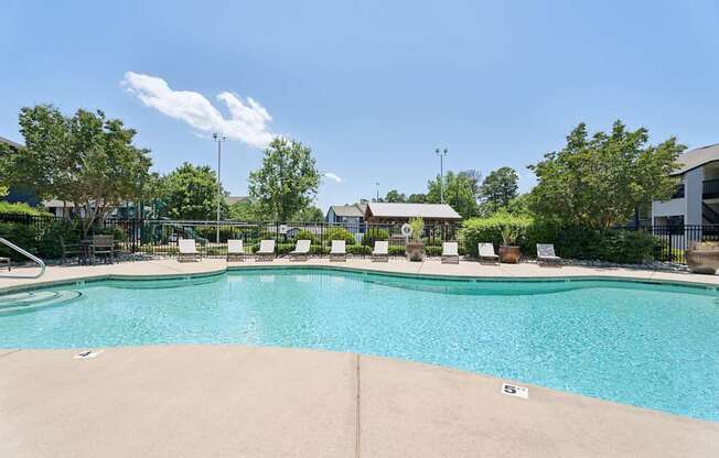 A large swimming pool surrounded by trees and lounge chairs.