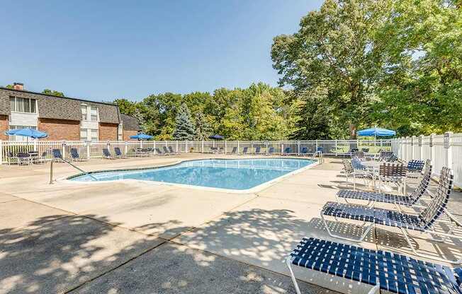 A sunny day at the pool with chairs and trees in the background.