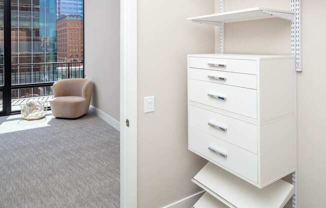 A white shelving unit with three drawers is in a room with a grey carpet.