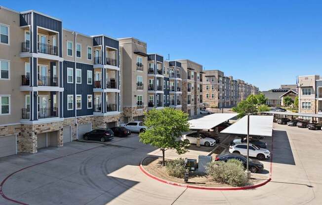 A view of apartment buildings with cars parked in the driveway.