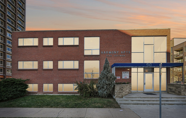 Charming brick facade of Harmony Apartments at sunset, showcasing modern windows and inviting entryway.