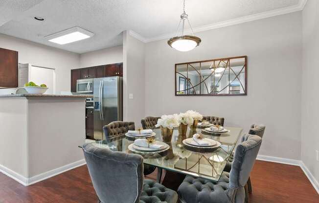 A dining room with a glass table and grey chairs.