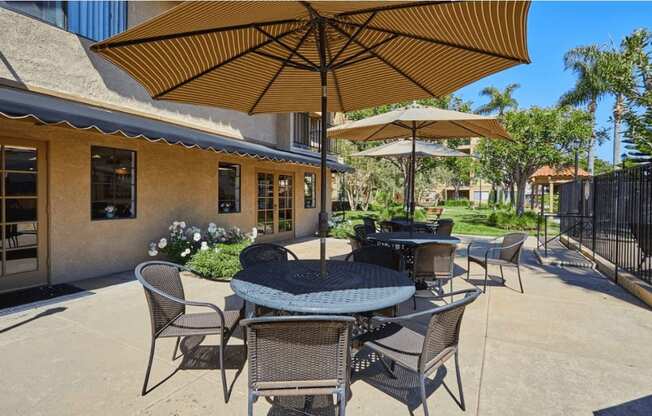 a patio with tables and umbrellas in front of a building at Huntington Terrace North Senior, Huntington Beach, CA