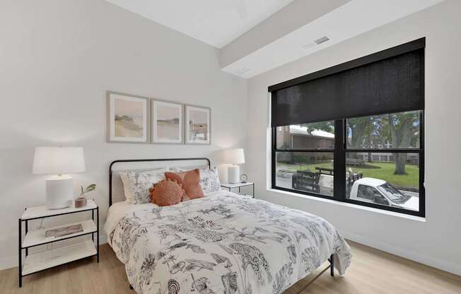 A bedroom with a large bed and a window showing a car and trees outside.