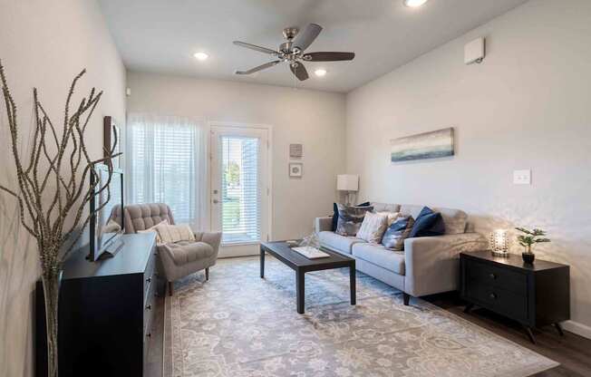 A living room with a grey couch, a black side table, and a ceiling fan.