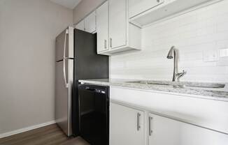A black refrigerator is in a kitchen with white cabinets.