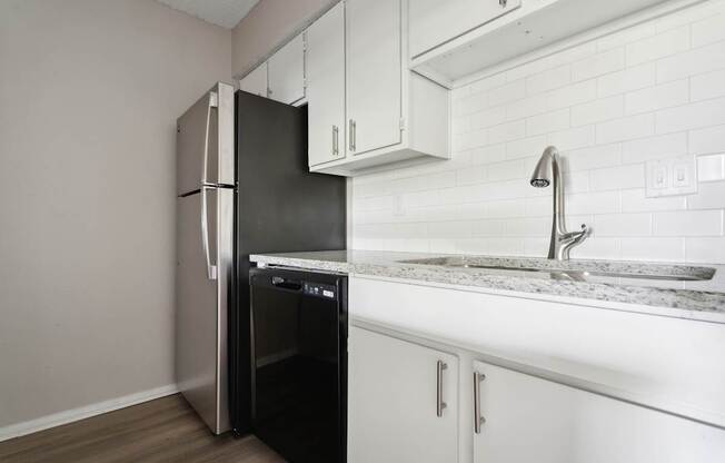 A black refrigerator is in a kitchen with white cabinets.